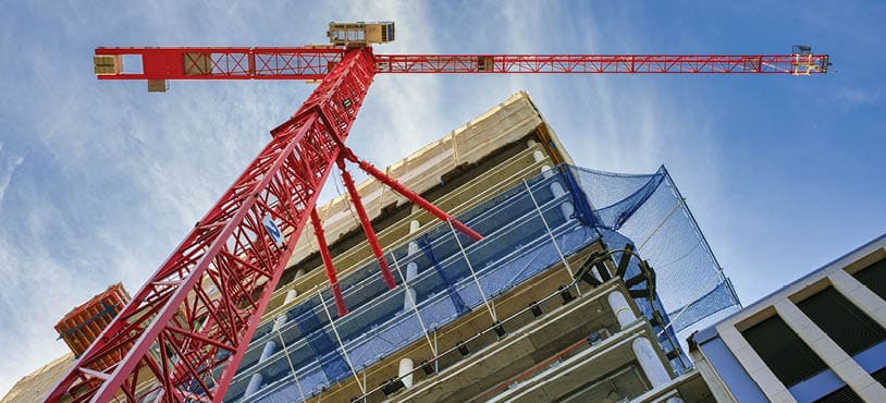 Looking up at the construction site of a high-rise building with red crane in the foreground.