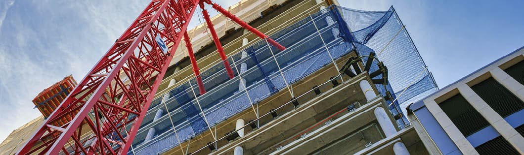 Looking up at the construction site of a high-rise building with red crane in the foreground.